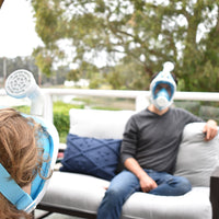 Two friends outside on a patio, wearing their Narwall Masks while sitting on a couch.